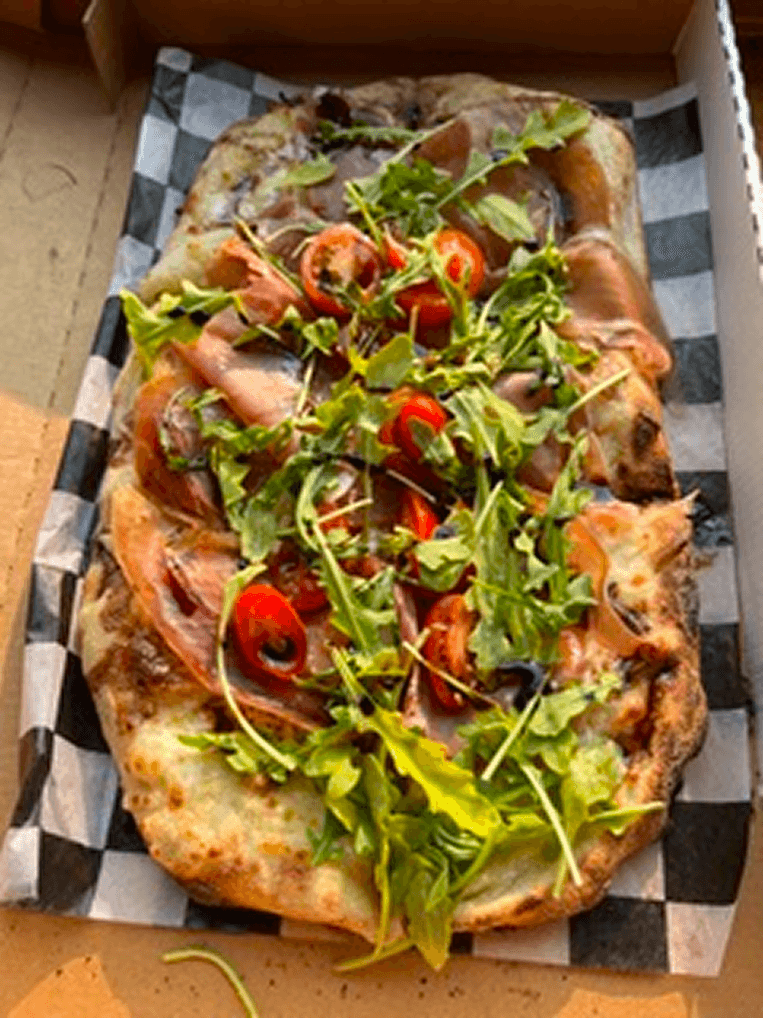 Prosciutto di Roma pizza topped with arugula, cherry tomatoes, prosciutto, and a balsamic glaze